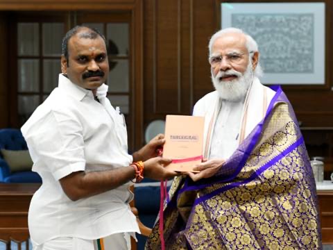 Dr. L. Murugan presents a copy of the Thirukkural to Prime Minister Narendra Modi, who wears a purple and gold shawl