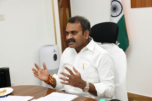 Dr. L. Murugan, seated at a desk with papers, speaks and gestures with both hands