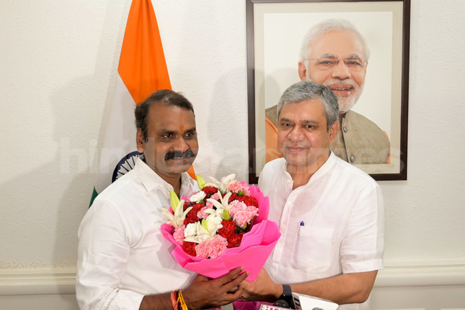 Dr. L. Murugan receives a bouquet from Shri Ashwini Vaishnaw beneath a framed portrait of the Prime Minister, with the national flag beside them