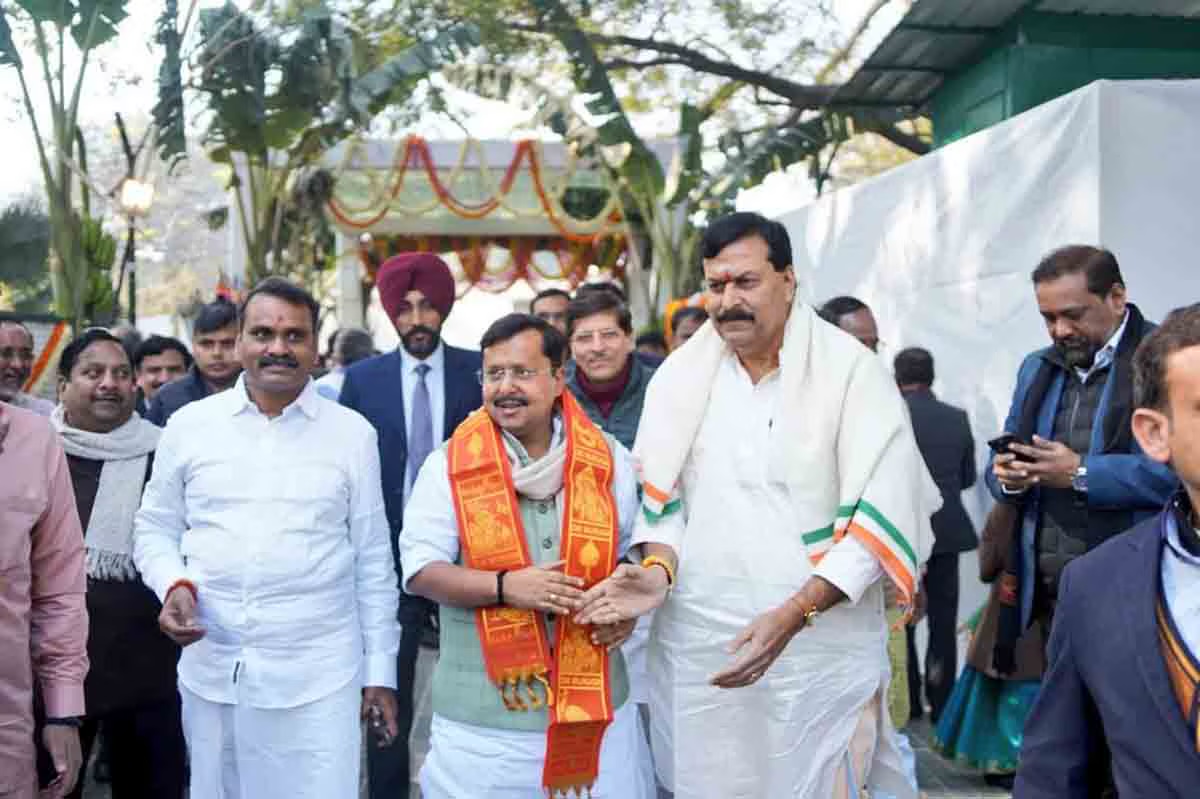Dr. L. Murugan walks with guests, one wearing a saffron stole, at an outdoor Pongal celebration decorated with marigold garlands